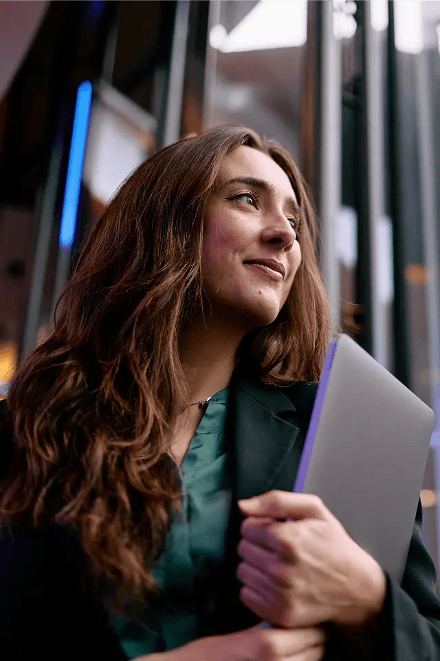 Woman holding a laptop looking wistfully to the left