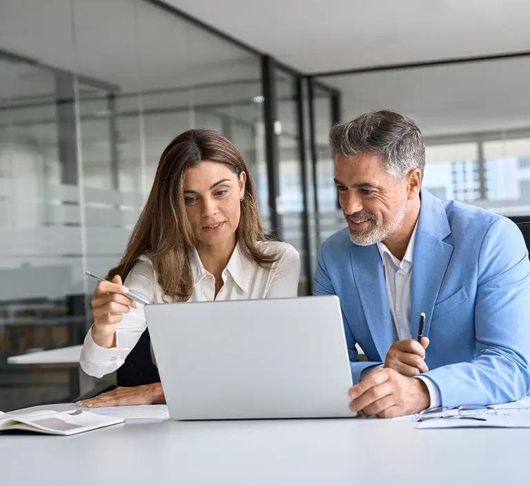 Male and female at a desk looking at a laptop and smiling